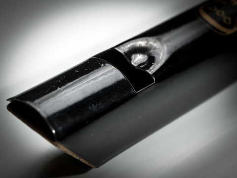 A black tin whistle lying on a white reflective surface