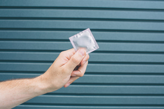 A picture of man's hand holding packed condom. Isolated on striped and blue background.