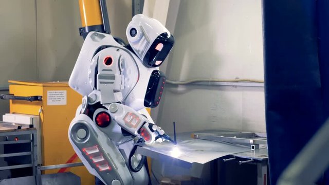 Android uses factory equipment to work with metal, close up. One robot works at a factory, welding with a tool.
