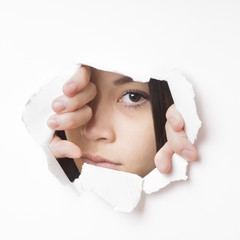 young asian woman tearing hole in paper wall to peek through