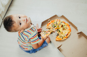 charming boy sitting on the floor eating pizza