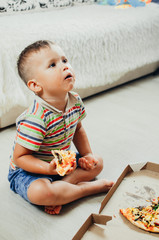 charming boy sitting on the floor eating pizza
