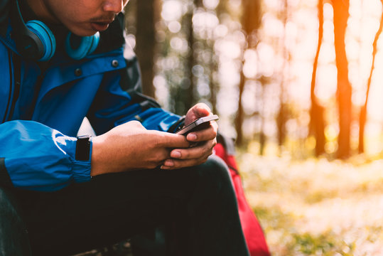 Traveler man backpacker using a smart phone in forest with sunlight