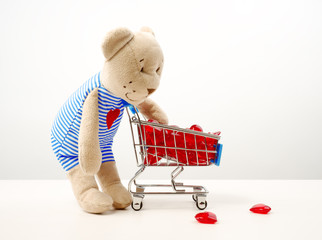 Teddy bear toy is pushing the trolley cart with red model hearts.Isolated on white
