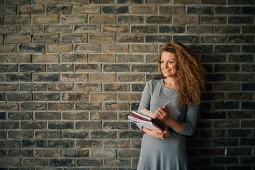 Portrait of woman holding books in front of brick wall.