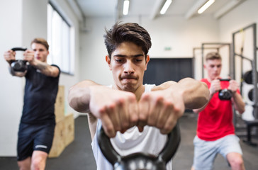 Naklejka premium Three young men in gym doing kettlebell swings.
