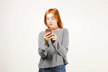 Portrait of surprised natural redhead woman wearing grey oversized loose shirt & hipster cat eye sunglasses staring at cell phone screen. Hipster female, eyes wide open. Isolated copy space background