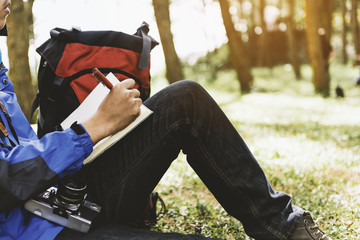 Young man with notebook and pen in his hand in the forest.Holiday or traveler concept with sunlight