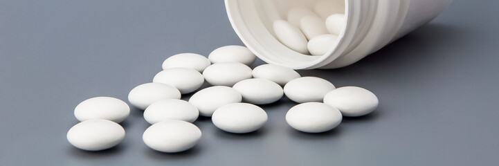 White round pills scattered from a white jar on a gray background.