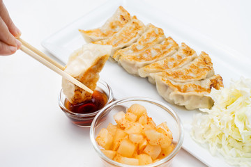 hand with chopsticks holding a piece of  gyoza fried - dumplings snack , with soy sauce