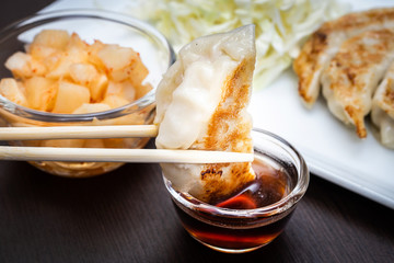 hand with chopsticks holding a piece of  gyoza fried - dumplings snack , with soy sauce