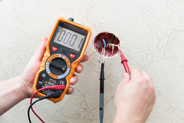 Close-up of man measuring and cheking power supply voltage with digital multimeter