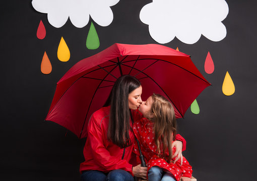 A small girl with her mother under an umbrella on a black background.