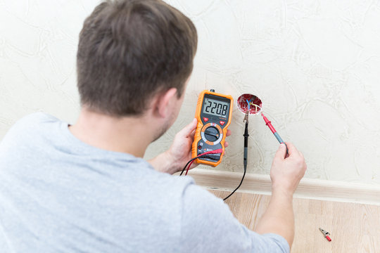Close-up of man measuring and cheking power supply voltage with digital multimeter