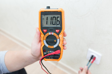 Close-up of man measuring and cheking power supply voltage with digital multimeter