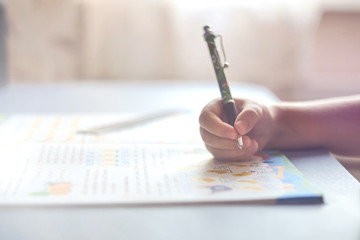 Close up kid's hand, girl holding pen doing homework