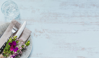 Rustic table setting with purple flowers on light wooden table.