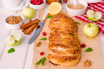 Apple pie with dried cherries, walnuts, lemon zest and cinnamon on white wooden background