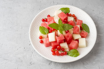 Salad of fresh juicy pieces of watermelon, melon, red currant and mint leaves on a plate.