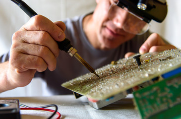 A male engineer is repairing an electronic board. Measurement of parameters and soldering of the electronic board.