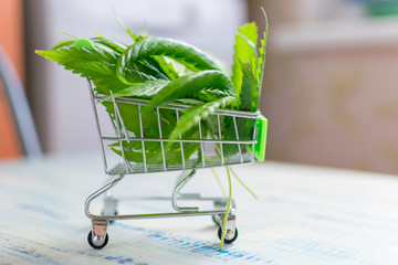 Buying, selling hemp. A shopping trolley with cannabis leaves on a wooden background.