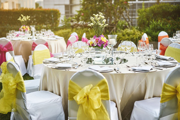 Wedding reception dinner table setting with flower decoration and white cover chairs yellow sash