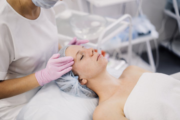 The hands of the cosmetologist on the face of the patient