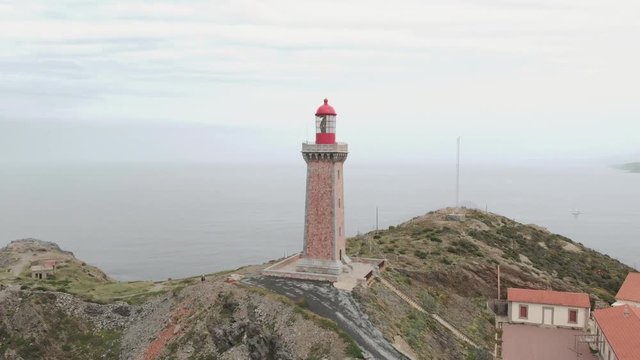 Wide aerial shot of lighthouse on the coast above the ocean in Catalonia, Spain