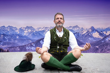 bavarian man sitting on front of mountains and meditating