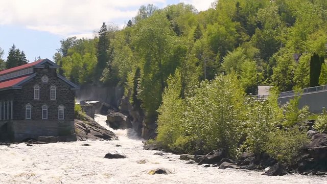 Panning of La Pulperie de Chicoutimi Regional Museum Pulp mill in Saguenay, Quebec, Canada with river and water current flowing in summer