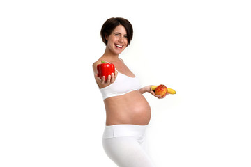 Schwangere Frau hält eine Paprika in der einen und eine Apfel und eine Banane in der anderen Hand