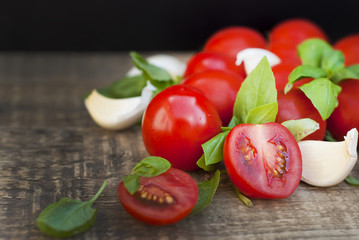 Fresh cherry tomatoes on rustic wooden board. Basil leaves and garlic in the background. Healthy food ingredients.
