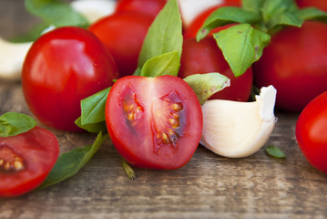 Fresh cherry tomatoes on rustic wooden board. Basil leaves and garlic in the background. Healthy food ingredients.