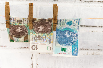 Three Polish zloty bills attached with old wooden washing clips hanging on the string on the white shabby bricks background
