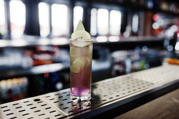 Alcoholic long violet cocktail with ice in glass at bar table.