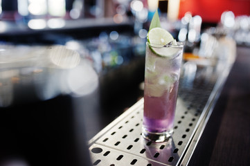 Alcoholic long violet cocktail with ice in glass at bar table.