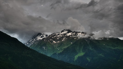 dramatische Berglandschaft mit dunklen Wolken, Berggipfeln mit Schnee und Wald in Bramberg am Wildkogel
