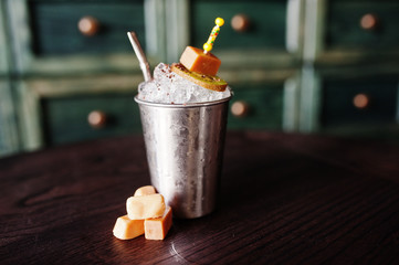 Alcoholic cocktail with sweets and candies in small silver bucket at bar table.
