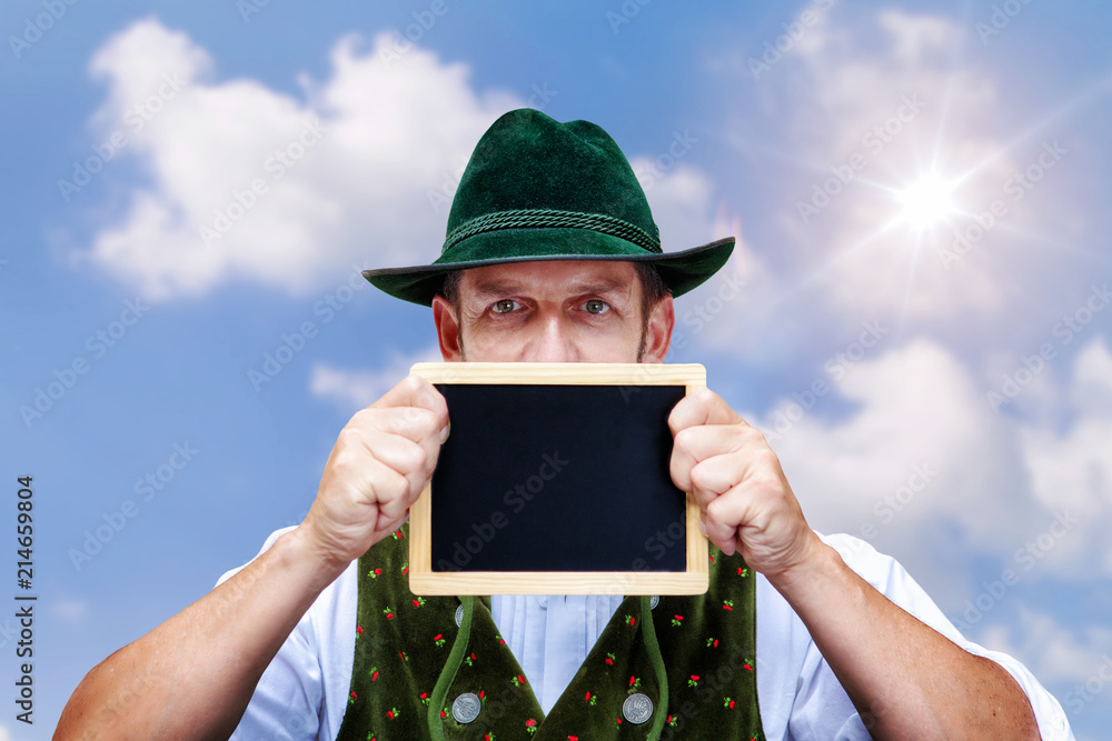 Wall mural bavarian man holding a blackboard  outdoors with blue sky