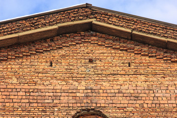 Triangular roof of an old building of orange bricks against a blue sky