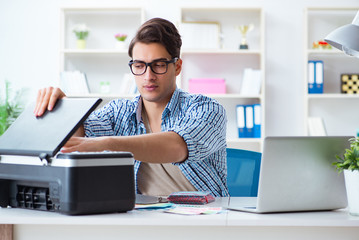 Young man employee working at copying machine in the office 