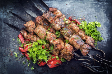Traditional Russian shashlik on a barbecue skewer with paprika as closeup on an old board