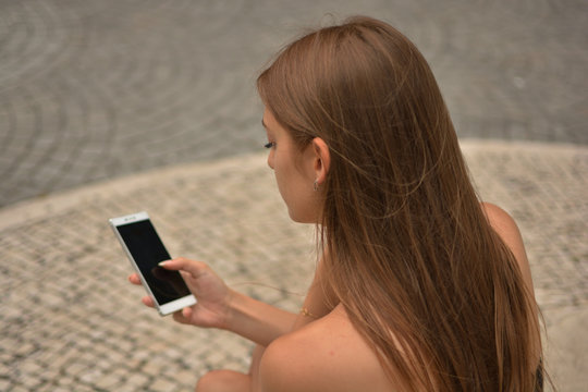 Chica joven atractiva chateando o mandando mensajes por el m&oacute;vil / smartphone sentada en una calle de la ciudad 