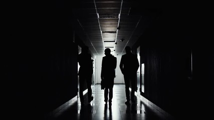Silhouettes of three businessmen walking in direction of light along the corridor. The end of working day. Team completed the work on project. Businessman go to meeting. 