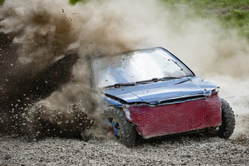 The car turns at a high speed on a gravel road raising dust and debris