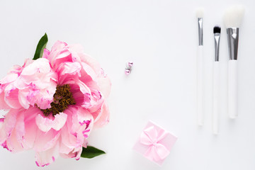 White background with copy space, pink peony flower, earrings, makeup brushes, small gift for girl, advertising space, top view