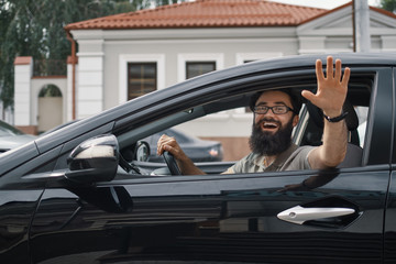 Cheerful man waving while driving a car