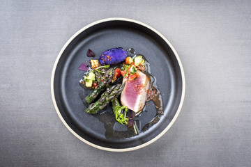 Modern fried tuna fish filet with green asparagus blue potatoes und vegetable chili relish as top view on a plate with copy space