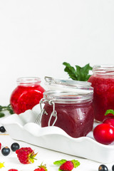 assortment of jams, seasonal fresh berries and fruits on white background