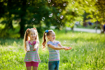 two beautiful little girls in the summer playing in the park with soap bubbles